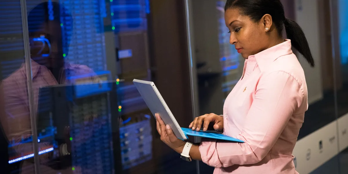 An engineer works on a laptop beside server racks in a data center.
